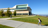 College of San Mateo against a clear blue sky with student carrying a backpack and walking up the hill